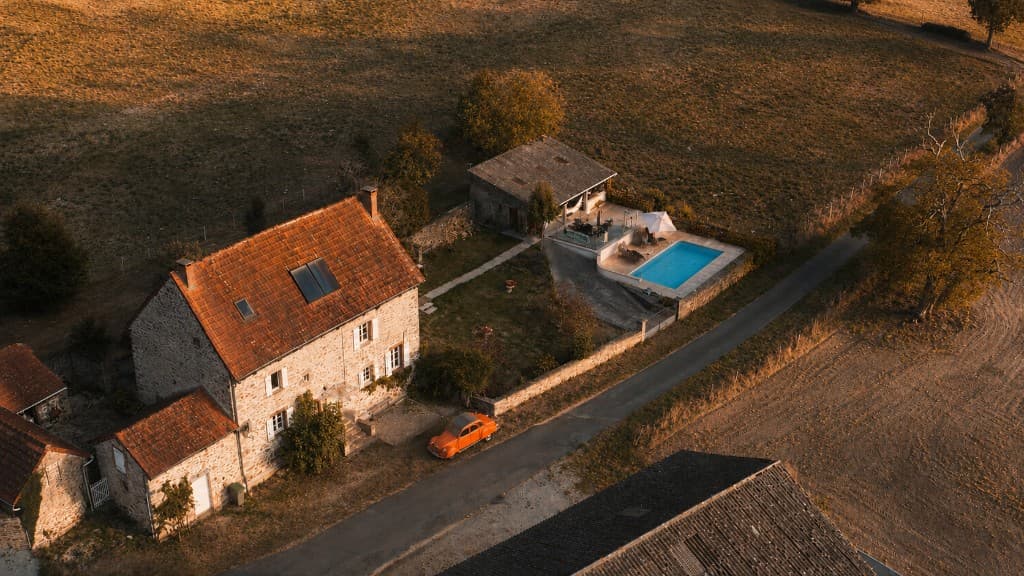 Aerial view of La Terrade at golden hour — stone farmhouse, garden, pool, and Limousin countryside